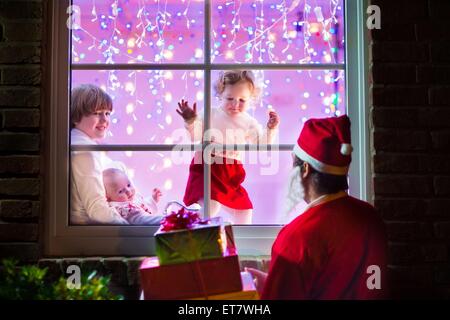 Trois enfants, happy boy holding petit bébé et un adorable bébé fille robe d'hiver en regardant leur père à Santa costume Banque D'Images