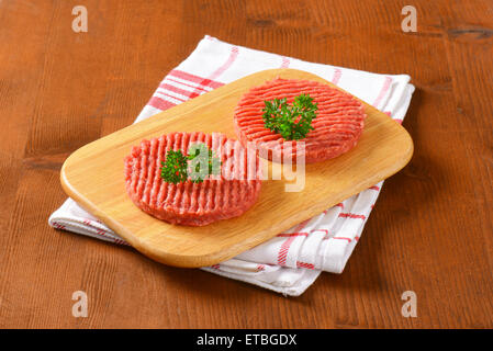 Deux pâtés de bœuf cru avec du persil sur planche à découper en bois et torchon à carreaux Banque D'Images