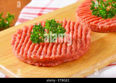 Détail de deux pâtés de bœuf cru avec du persil sur planche à découper en bois Banque D'Images