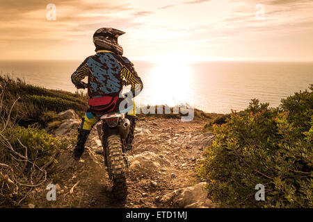 Enduro racer assis sur sa moto en regardant le coucher du soleil. Banque D'Images