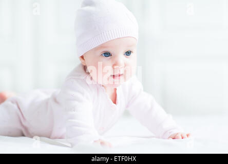 Curieuse petite fille couchée sur son ventre portant chapeau tricoté rose Banque D'Images