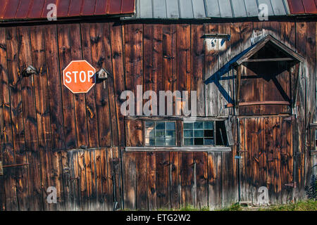 Le côté d'une vieille grange en bois sombre, avec des bois de couleur brun-rougeâtre, maisons d'oiseaux, panneau d'arrêt et de vieilles fenêtres. Dans l'étude de la texture. Banque D'Images