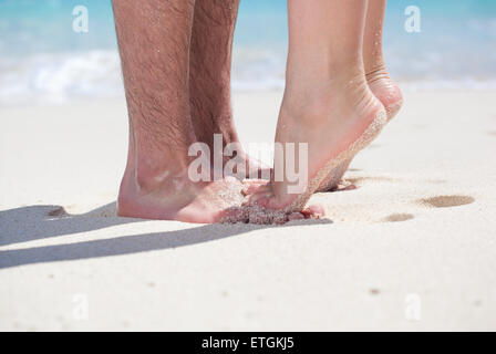 La femme debout les jambes pieds nus pieds libre à pied mâle et s'embrasser sur une plage de sable avec une mer turquoise background, pas de visage. Banque D'Images