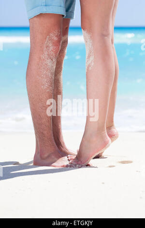 La femme debout les jambes pieds nus pieds libre à pied mâle et s'embrasser sur une plage de sable avec une mer turquoise background, pas de visage. Banque D'Images