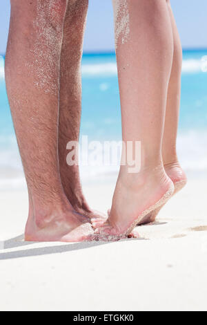 La femme debout les jambes pieds nus pieds libre à pied mâle et s'embrasser sur une plage de sable avec une mer turquoise background, pas de visage. Banque D'Images