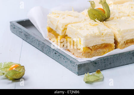 Des tranches de gâteau avec des fruits tropicaux et mousse crémeuse et mangue physalis servi en plateau en bois sur fond bleu clair Banque D'Images