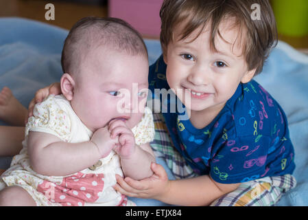 Un garçon de 2 ans et sa soeur nouveau-né assis sur un lit. Banque D'Images