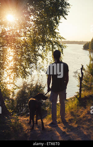 Homme avec une promenade de chiens dans le coucher du soleil au bord du lac Banque D'Images