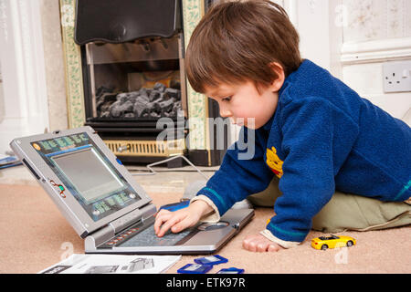 Jeune enfant, garçon, 3-4 ans, à l'intérieur à genoux sur le tapis, la lecture attentive de l'enfant avec V-Tech ordinateur portable, l'apprentissage de base compétences informatique Banque D'Images