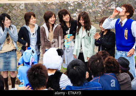 Japon, Shukugawa. Soirée printanière de cerisiers en fleurs d'étudiants. Plusieurs se tenant debout à regarder un homme qui dédoit un verre en une seule fois, une partie d'un jeu d'étudiant. Banque D'Images