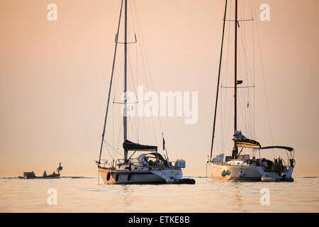 Deux bateaux ancrés dans la mer au coucher du soleil avec une petite embarcation à moteur voile en arrière-plan en Rovinj, Croatie. Banque D'Images