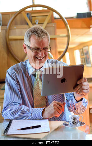 ZOOM iPad homme d'affaires en ligne équipes Skype rencontre homme d'affaires mature en interaction avec son iPad air Smart Tablet PC seul dans son bureau de péniche Banque D'Images