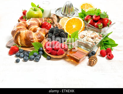 Petit-déjeuner sain avec des croissants, de muesli, de baies fraîches, fruits orange, pomme, lait. Concept d'aliments biologiques Banque D'Images