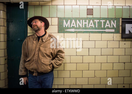 Man with hat standing next to Manhattan inscription faite de vieilles tuile sur mur de métro à New York, New York, USA Banque D'Images