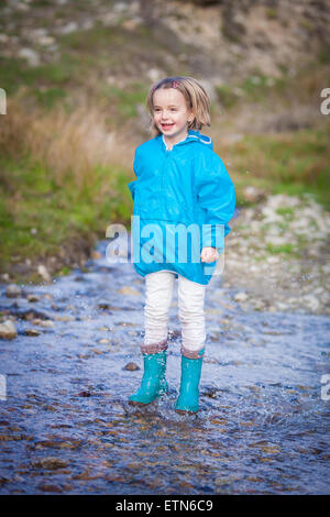 Smiling girl qui saute dans une flaque Banque D'Images