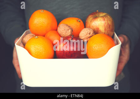 Portrait d'un homme tenant un bol de pommes, oranges et noix Banque D'Images