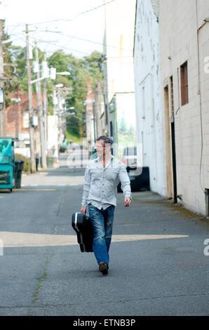 Homme avec étui à guitare Walking Down Alley, Port Angeles, Washington, USA Banque D'Images