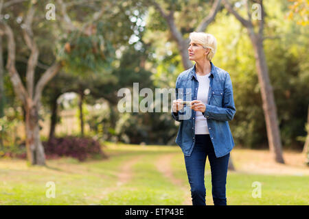 Thoughtful young woman holding camera outdoors Banque D'Images