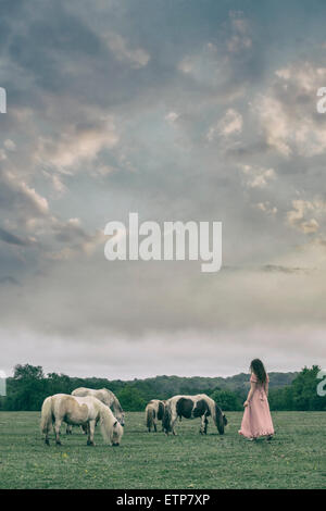 Une femme dans une robe rose est en marche vers certains poneys sauvages Banque D'Images