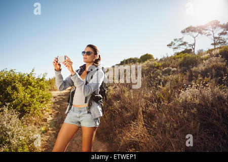 Image de jeune femme parlant des photos avec son téléphone portable lors d'une randonnée. Les femmes de race blanche randonnée sur une journée d'été. Banque D'Images