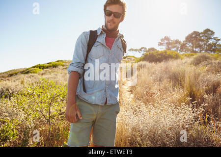 Portrait de beau jeune homme randonnée dans la nature. Caucasian man walking on country trail sur jour ensoleillé chaud. Banque D'Images