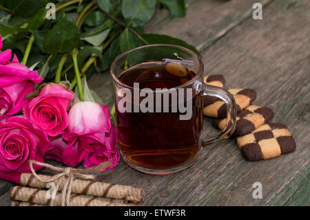 Verre de thé et biscuits sur une plaque avec un bouquet de roses Banque D'Images