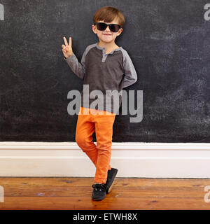 Longueur totale de tir cool little boy wearing sunglasses désignant la victoire. Jeune garçon de l'école dans les occasionnels montrant le symbole de paix Banque D'Images