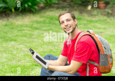 L'homme portait un jeans et t-shirt rouge assis sur l'herbe à la caméra à smiling Banque D'Images