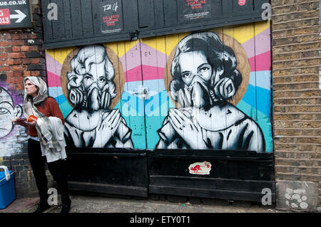 Une femme portant un foulard se place en avant d'un morceau de l'art de rue montrant deux femmes avec des bombes aérosols d'un masque de visage par Zabou Banque D'Images