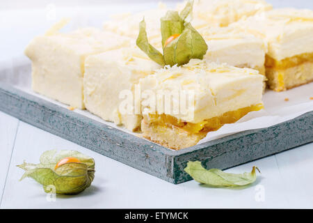 Des tranches de gâteau avec des fruits tropicaux et mousse crémeuse et mangue physalis servi en plateau en bois sur fond bleu clair Banque D'Images