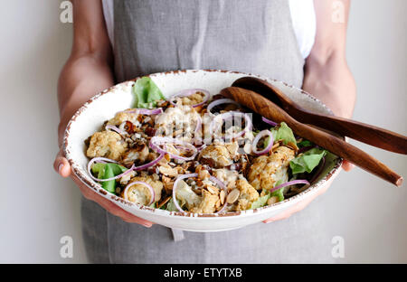 Une femme tient un grand bol d'une salade faite de chou-fleur rôti, lentilles, les dates, les oignons, et les dates et arrosé avec ta Banque D'Images