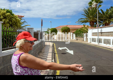 Jusqu'à la taille en portrait de profil tanné senior smiling blonde dame en bonnet rouge que toucher sa main sur street of tropical vi Banque D'Images