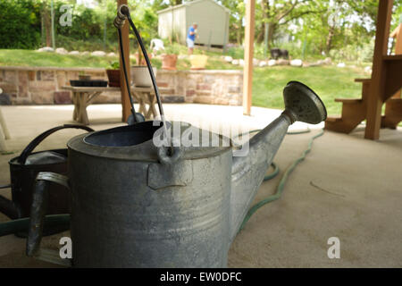 Arrosoir en aluminium sur le porche, en premier plan avec l'homme en arrière-plan qui travaillent dans le jardin. USA. Banque D'Images