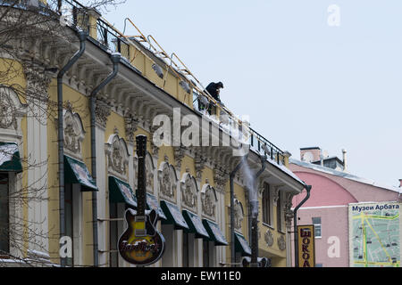 Un travailleur non identifiés, méconnaissable supprime la neige de la toiture de l'ancien bâtiment dans la rue Arbat de Moscou Banque D'Images