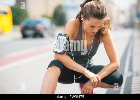 Une femme portant des écouteurs et son appareil dans un brassard sur son bras est en regardant le sol, écoutant attentivement les m Banque D'Images