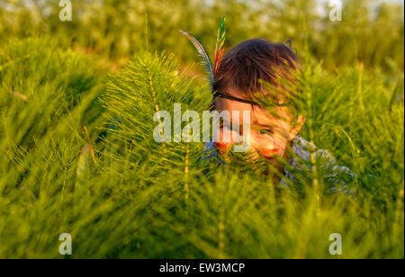 Funny little girl comme indiennes se cacher derrière l'herbe Banque D'Images