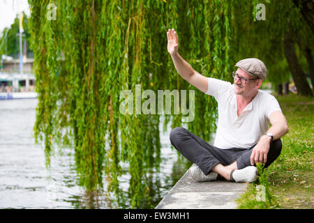 Homme assis près de l'eau dans un parc et en agitant à quelqu'un Banque D'Images
