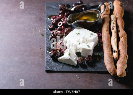 Ensemble et olives noires et le bloc de fromage feta à l'huile d'olive et des grissini gressins sur ardoise noire sur dar Banque D'Images