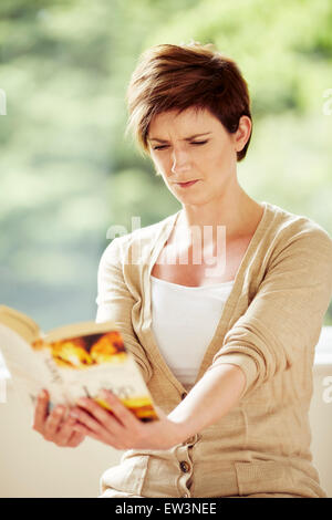 Femme avec une mauvaise vision de la difficulté à lire livre Banque D'Images