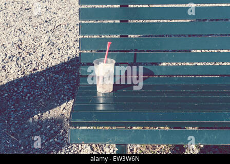 Boissons en plastique jetables tasse avec paille couché sur banc. Banque D'Images