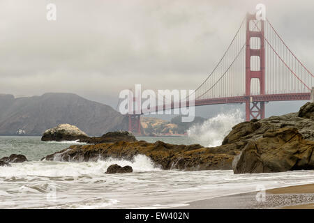Rochers noirs et les vagues de l'océan sur Baker Beach comme le Golden Gate Bridge dans le brouillard sur le contexte à San Francisco, USA. Banque D'Images