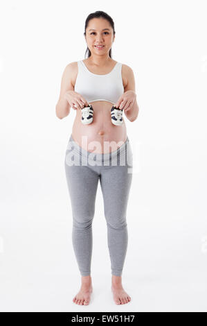 Femme enceinte tenant une paire de chaussures de bébé et souriant à la caméra, Banque D'Images