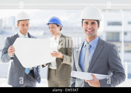 Les hommes d'affaires et une femme avec un casque et holding blueprint Banque D'Images