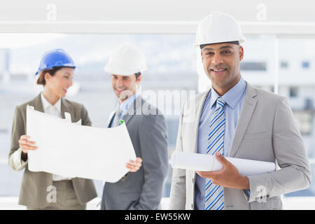 Les hommes d'affaires et une femme avec un casque et holding blueprint Banque D'Images