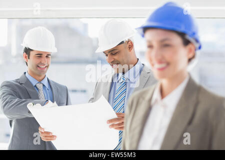 Les hommes d'affaires et une femme avec un casque et holding blueprint Banque D'Images