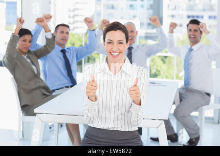 Smiling businesswoman giving Thumbs up avec son équipe derrière Banque D'Images