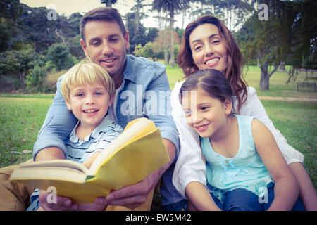 Famille heureuse de lire un livre dans le parc Banque D'Images