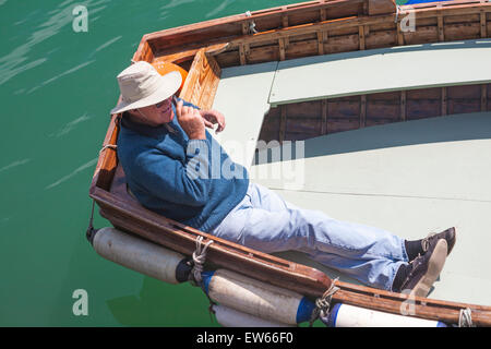 Homme Ferry sur téléphone mobile reposant sur l'aviron dans le soleil attendent des passagers à Weymouth, Dorset en Juin Banque D'Images