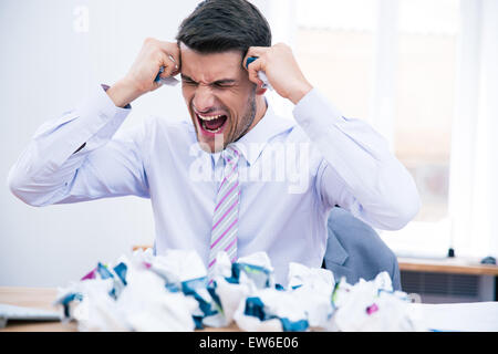 Angry businessman assis à la table avec du papier froissé et crier in office Banque D'Images