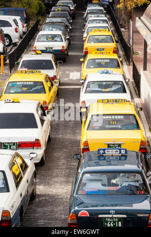 Vue en hauteur de la double rangée de taxis qui attendent sur la route, des taxis jaunes, noirs et blancs à l'extérieur de la gare (non représentés) , à Kurashiki au Japon. Banque D'Images